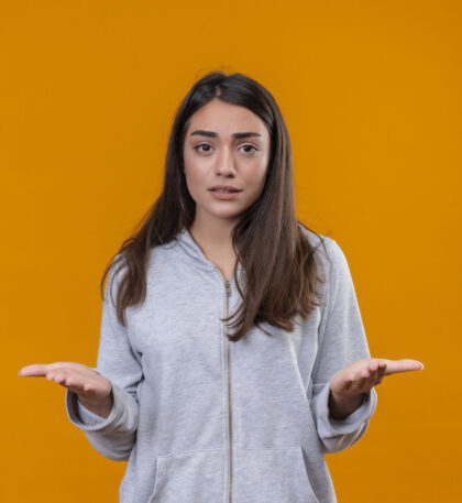 young beautiful girl in gray hoody in desperate emotion standing over orange background